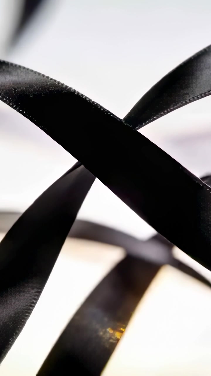 Vertical video: Shifting black satin ribbons crossing panel, showing warm band and gold flecks