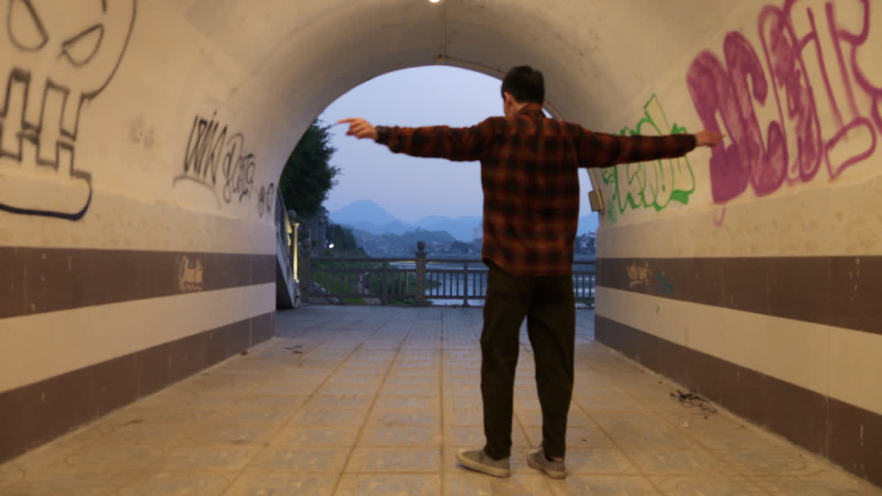 Uomo hipster asiatico che balla all'interno del tunnel con graffiti sui muri in Vietnam