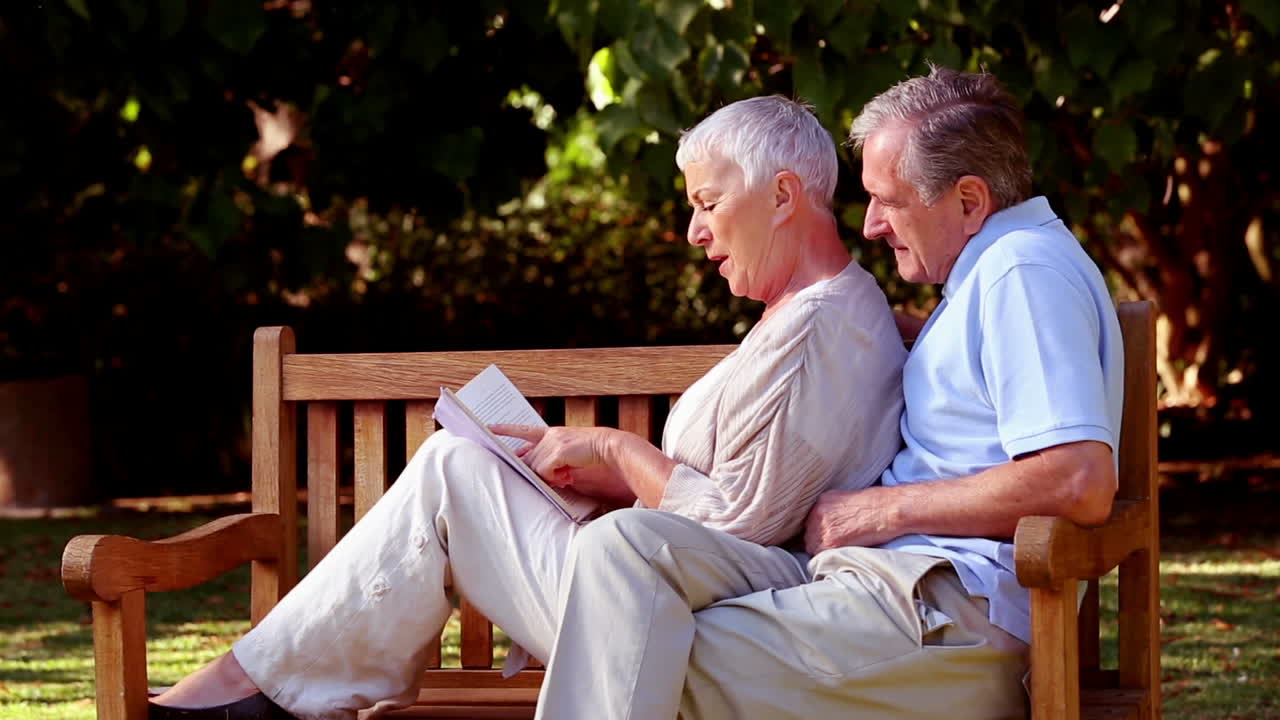 Wife leaning on husband on a bench and reading a book