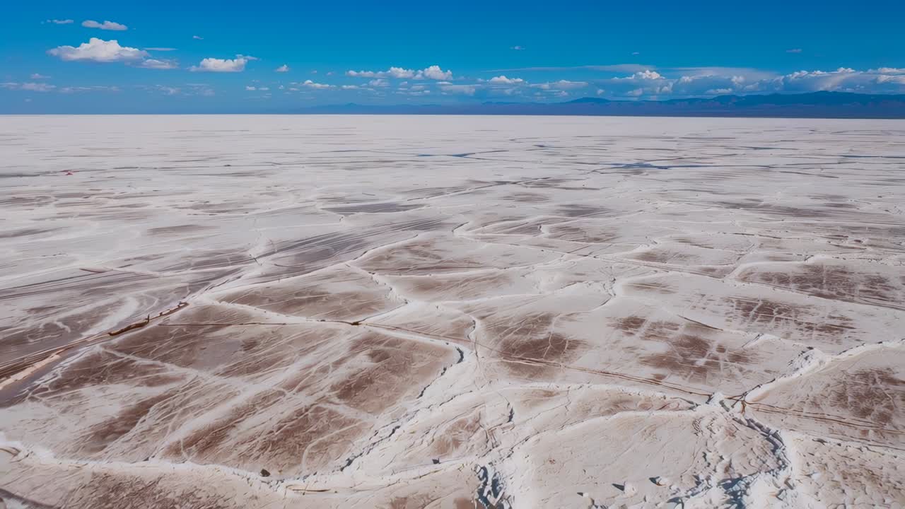 Drone subindo e revelando as salinas em uma planície desértica seca, examinando crostas poligonais e montanhas distantes