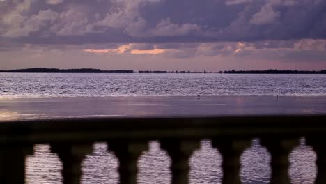 Nighttime-shot-of-birds-flying-across-still-water-with-silhouette-of-balcony-in-forground