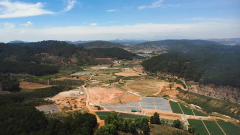 Aerial-drone-backward-moving-shot-with-huge-agricultural-field-surrounded-by-hilly-terrain-in-Tu-Tra,-Don-Duong-District,-Lam-Dong,-Vietnam-at-daytime