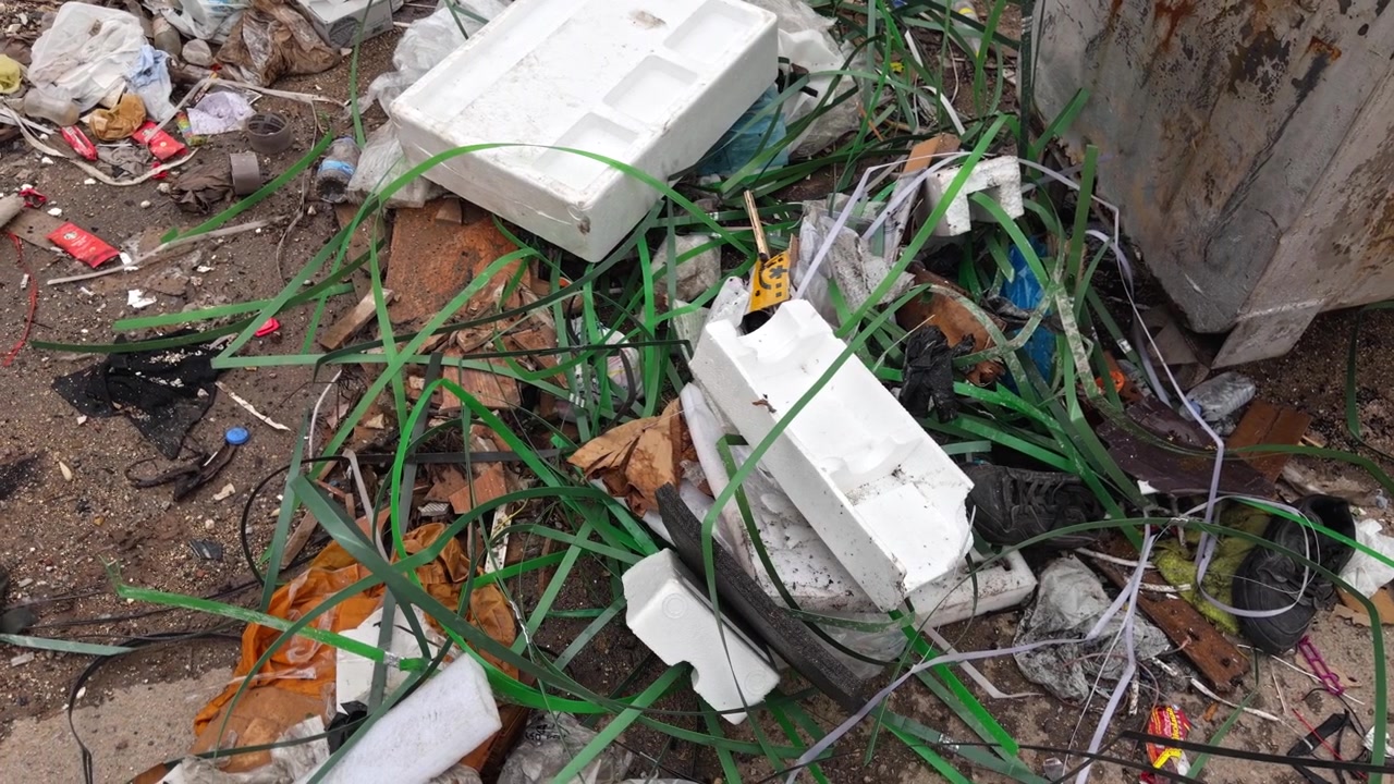 Kinoreifes 4K-Nahaufnahme-Filmmaterial von vermischtem Plastikmüll, Kabeln, Schaumstoff, Tüten und Schutt, der auf dem Boden verstreut ist. Filmmaterial zum Konzept der städtischen Umweltverschmutzung und des Umweltbewusstseins