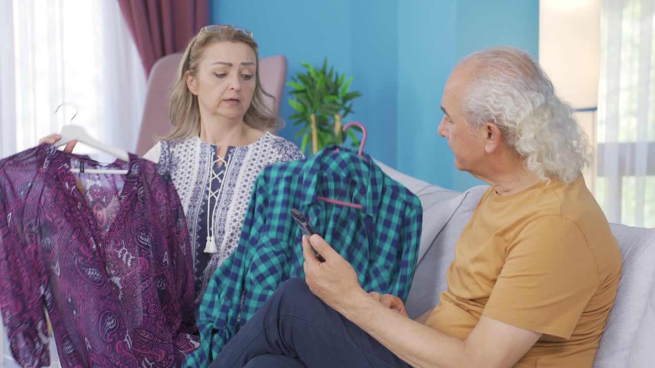 여자는 집에서 옷을 시도하고 남편은 그녀를 도와줍니다.