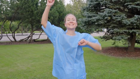 woman dancing joyfully by herself at the park while wearing blue lab coat