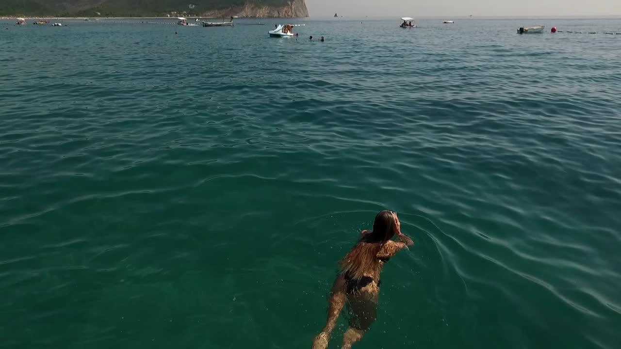 Girl in sea swims, areal footage goes up and shows sea water on a summer day