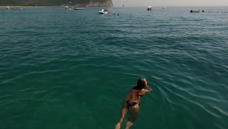 Girl-in-sea-swims,-areal-footage-goes-up-and-shows-sea-water-on-a-summer-day