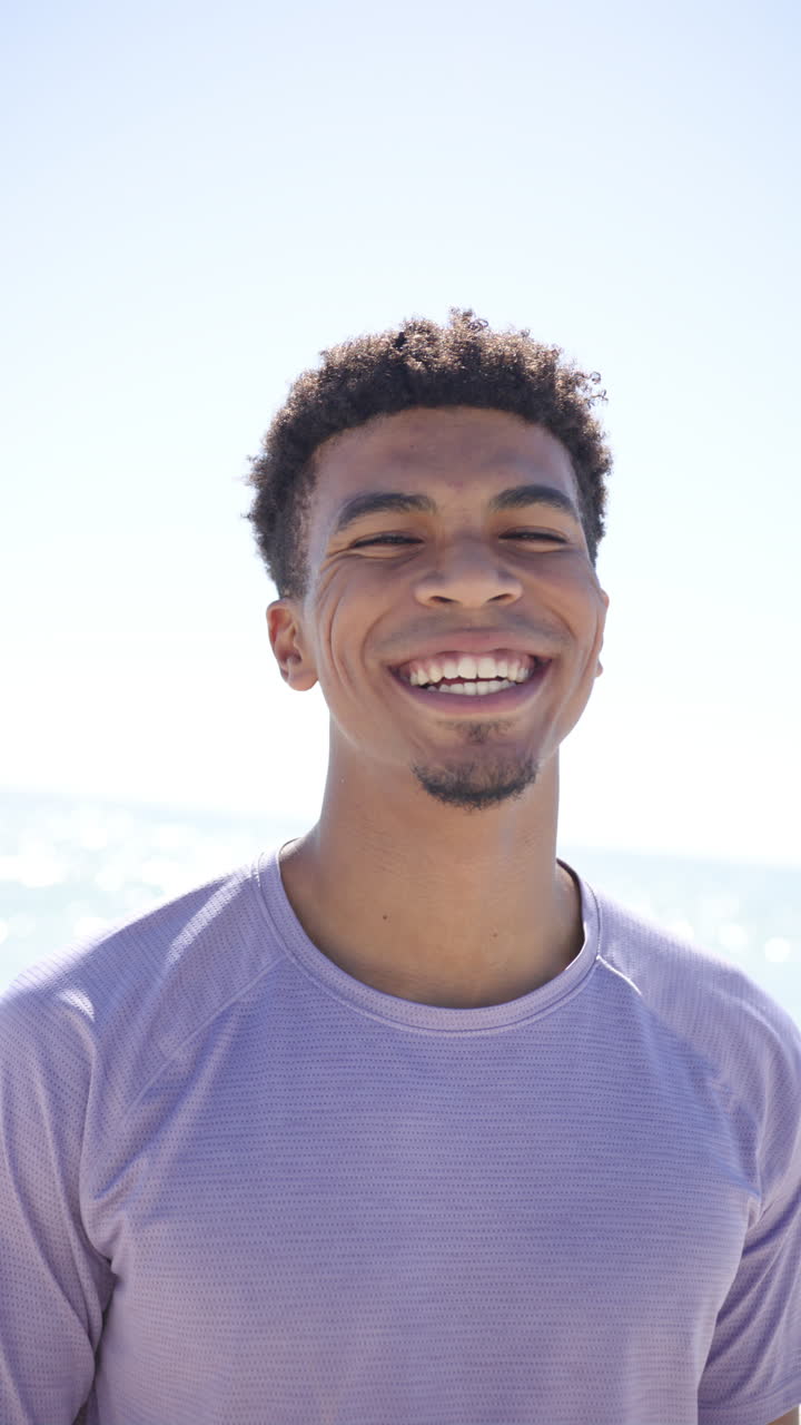 Vertical video: Smiling man enjoying sunny day at beach, wearing casual shirt