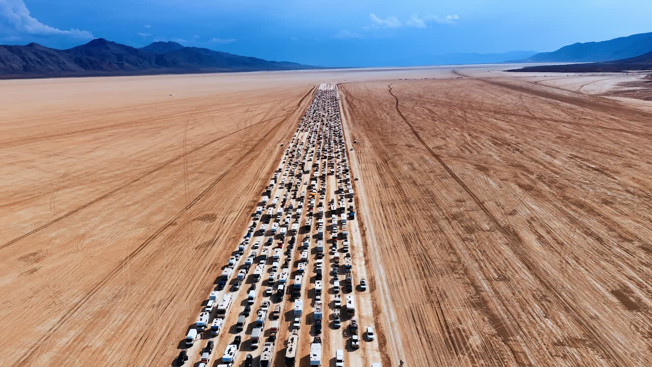 Long Line of Vehicles Crossing the Desert Playa. A dramatic, high-angle view shows an extremely long line of vehicles, including RVs and cars