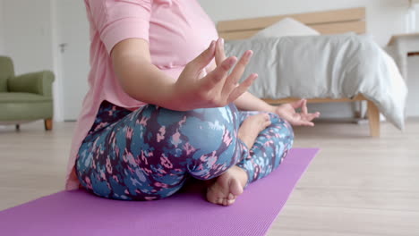 midsection of plus size biracial woman sitting on floor practicing yoga meditation, slow motion