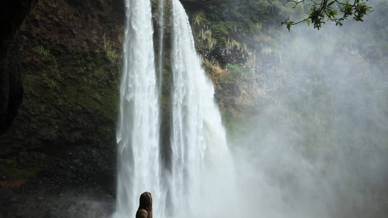 una mujer joven mirando una cascada en kauai, hawaii, cámara lenta