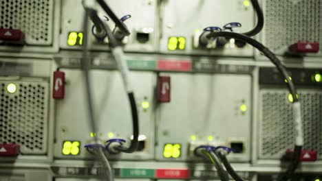 black cables in a datacenter room, plugged to many servers, rack focus