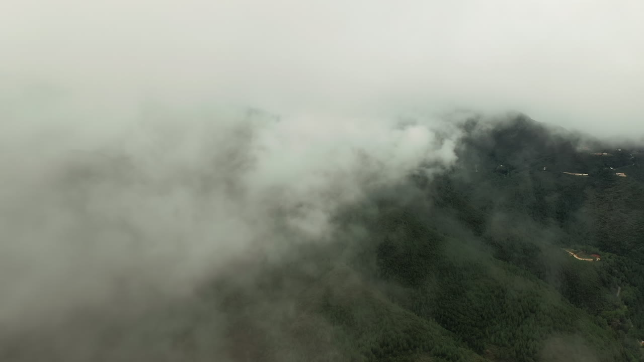 Aerial drone shot soaring through clouds over lush green mountains. The camera glides above the peaks, revealing dramatic landscapes and vibrant vegetation below.