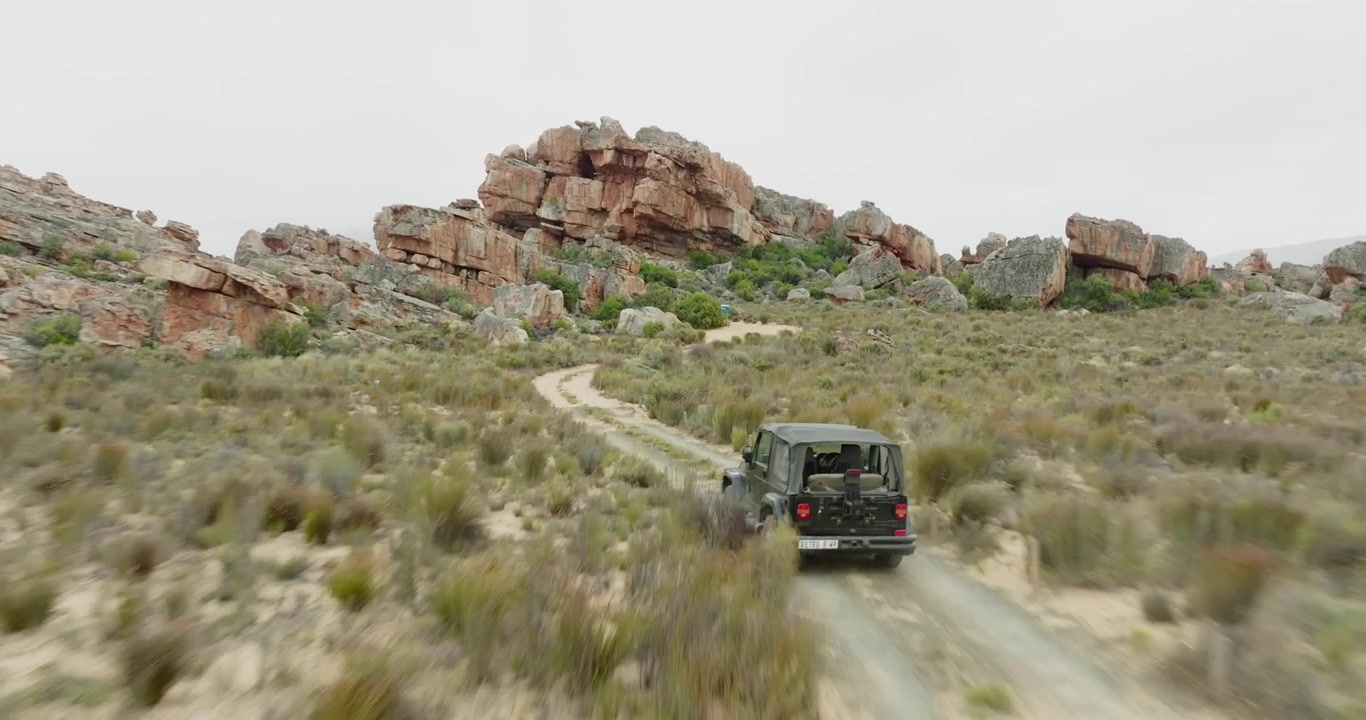 Drone voa rápido sobre paisagem desértica na Área Selvagem de Cederberg, África do Sul, e persegue um veículo off-road preto - paisagem cênica