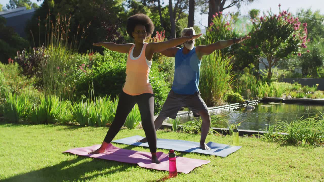 una pareja de ancianos afroamericanos haciendo ejercicio practicando yoga de pie en un jardín soleado