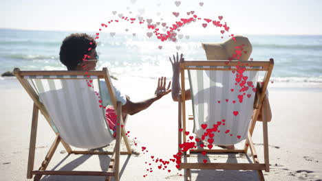 animation of hearts moving over diverse couple in love in deckchairs on beach in summer