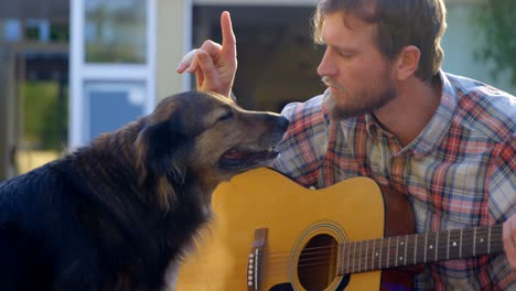 man with his dog playing guitar in the garden 4k