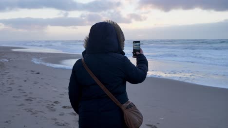 ズィルト島の美しいビーチで、風の強い日にスマートフォンでビデオを作成している若い女性のワイドショット