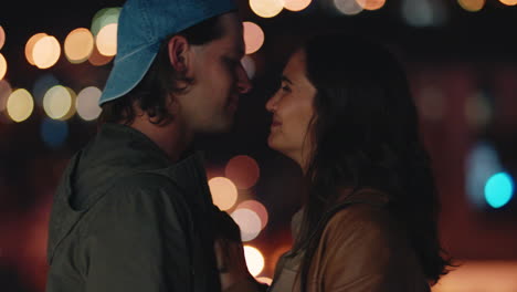 young caucasian couple kissing on rooftop at night enjoying romantic relationship embracing in peaceful urban evening watching beautiful city lights