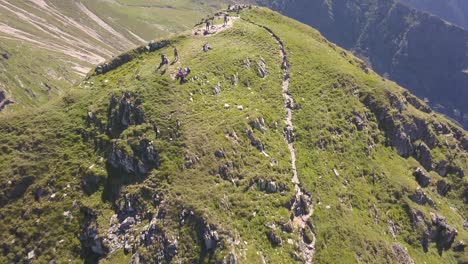 Ascending-aerial-view-of-hikers-on-top-of-mountain-after-reaching-the-summit-along-steep-narrow-rocky-path