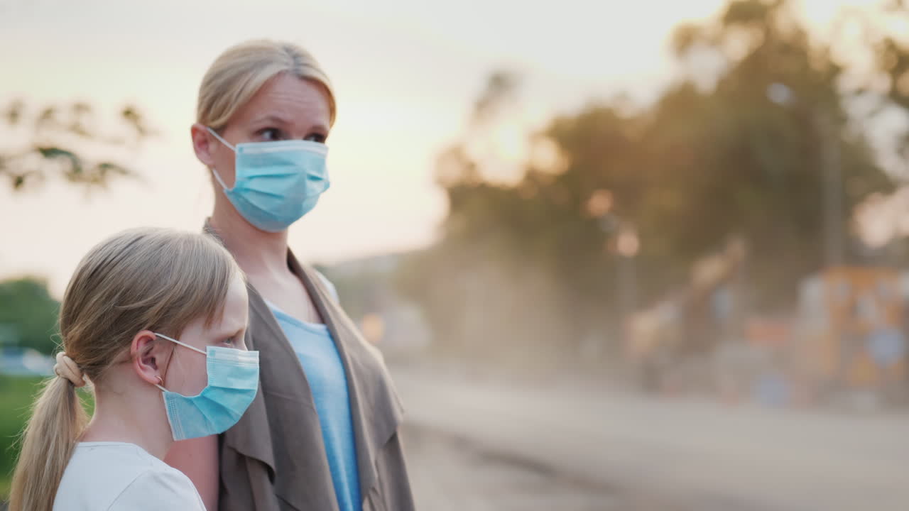 보호 마스크를 쓴 아이를 둔 여성이 도시의 먼지투성이 도로 근처에 서 있다