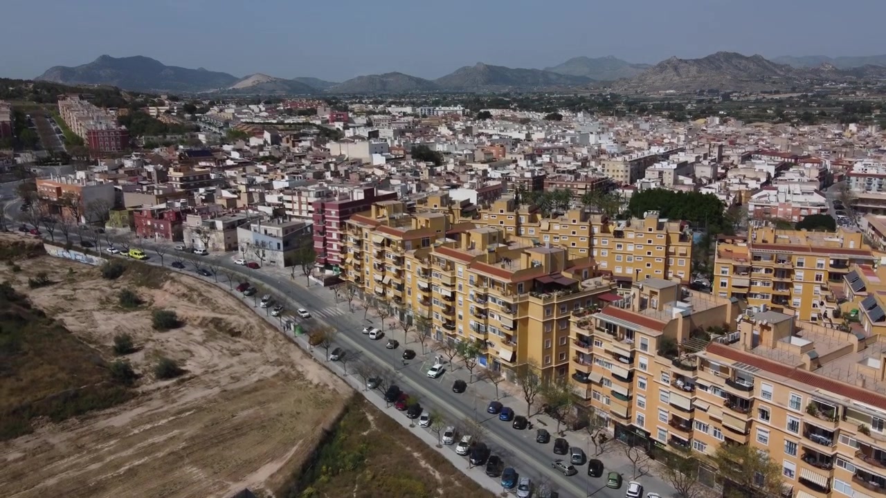 Tomada de drone capturando a vista aérea panorâmica da cidade de Aspe entrando pelo sudeste. Apresenta paisagem urbana, zona rural circundante e acesso rodoviário em Alicante, Espanha