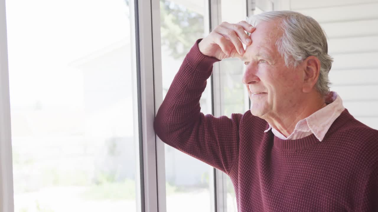 un hombre caucásico feliz tocando su cabeza y mirando por la ventana.
