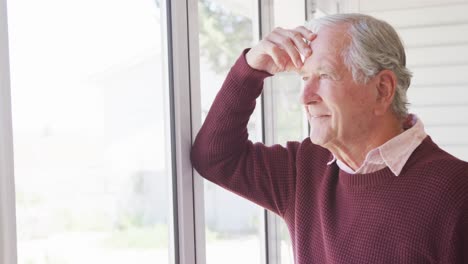 Happy-caucasian-senior-man-touching-his-head-and-looking-through-window