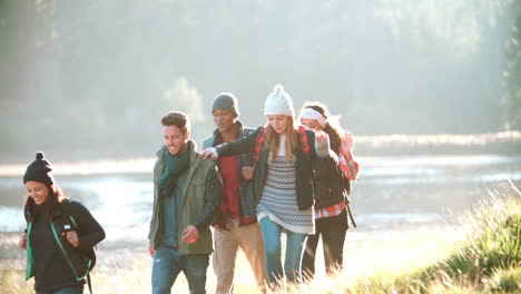 five friends on a camping trip walking in a row near a lake