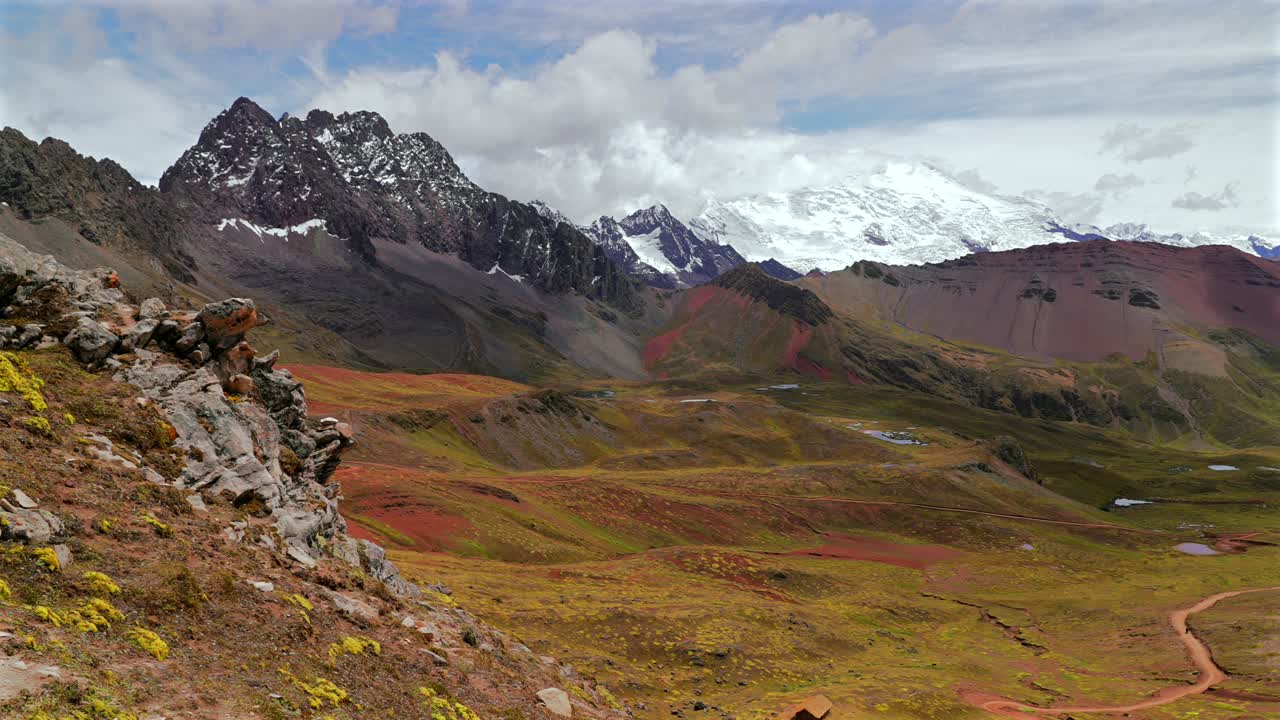 Vista paesaggistica della Montagna Arcobaleno Vinicunca in Perù, con il Ghiacciaio Ausangate e le montagne delle Ande peruviane della Cordigliera di Vilcanota vicino alle calotte glaciali di Quelccaya, sotto un cielo azzurro e soleggiato con nuvole mattutine e un panorama della valle.