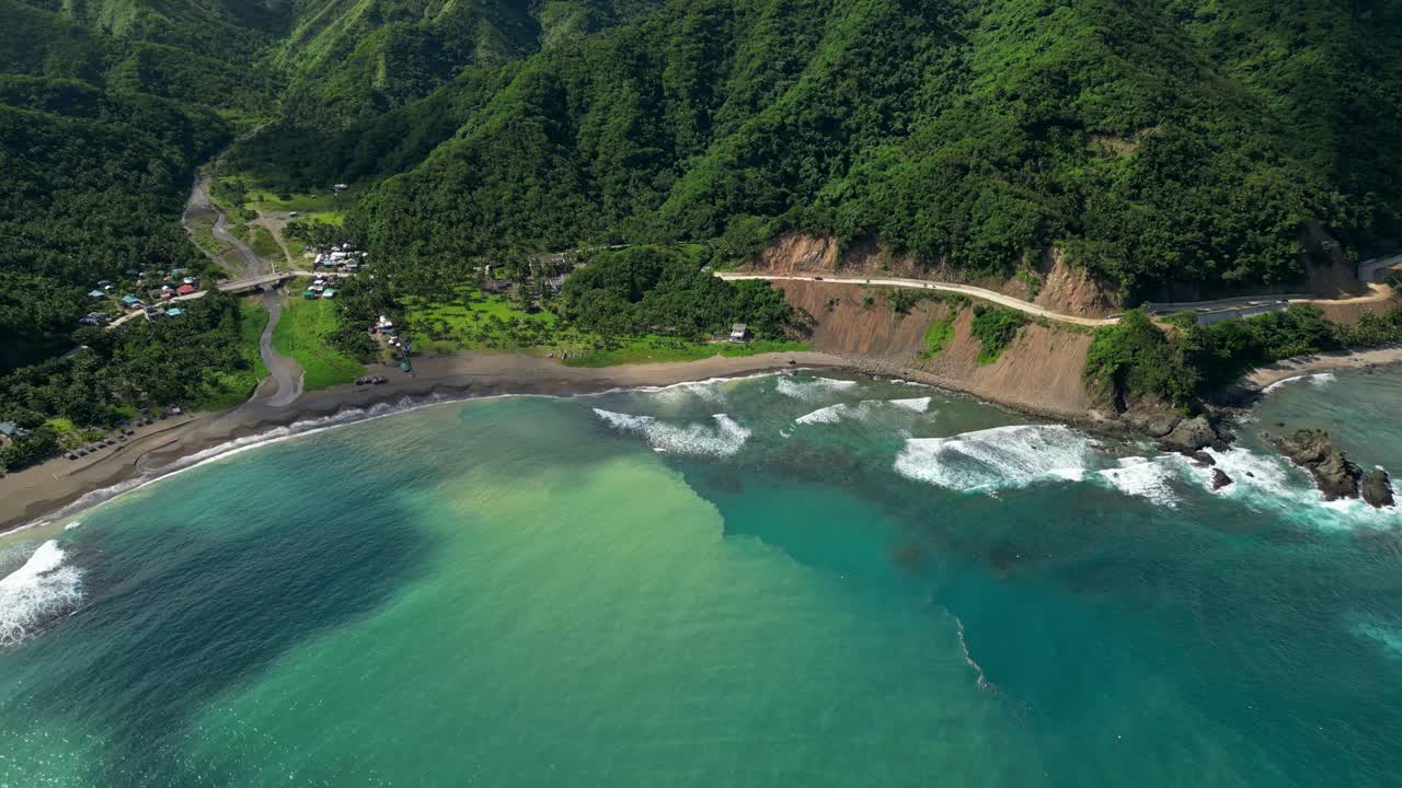 Pan aerial of Matawe, Dingalan, Aurora, showcasing the triangular hills and the yellow hillside road, opening to the vast sea where turquoise waves crash along the rugged coast