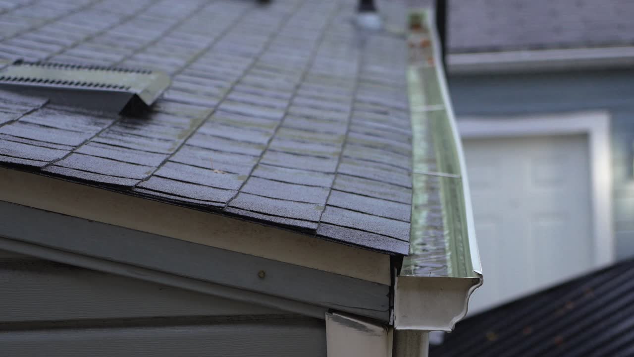 Calm rainy day clip showing raindrops on shingles and gentle runoff into a home gutter system