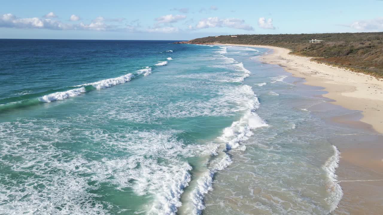 vuelo aéreo a lo largo de una playa soleada con olas rompiendo en la arena