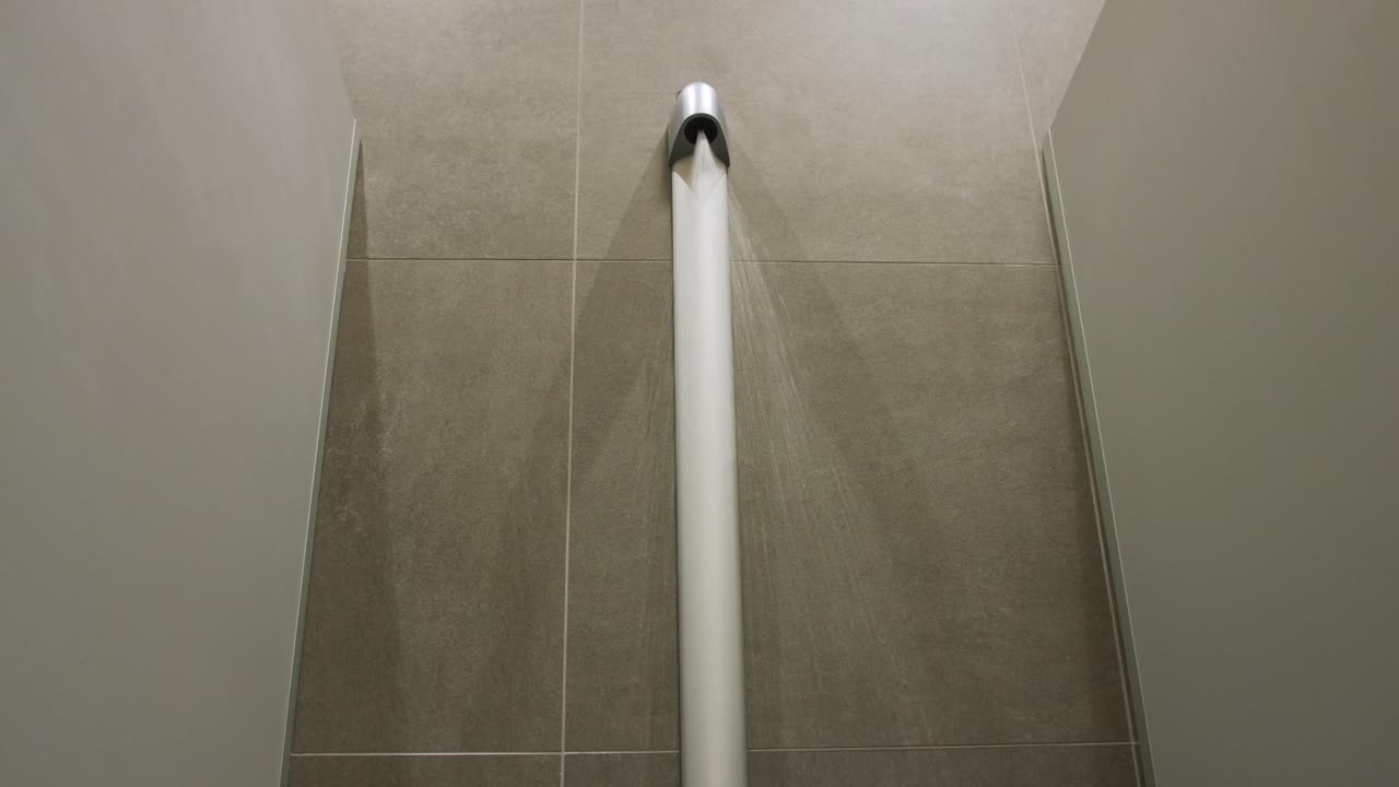 Captivating gimbal shot of water streaming down a sleek bath column in a modern tiled shower cabin