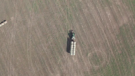 granjero agrícola que conduce una máquina tractora industrial verde que transporta balas de heno en el campo rural llanuras planas tierras de cultivo, saskatchewan, canadá, directamente sobre el descenso aéreo del círculo