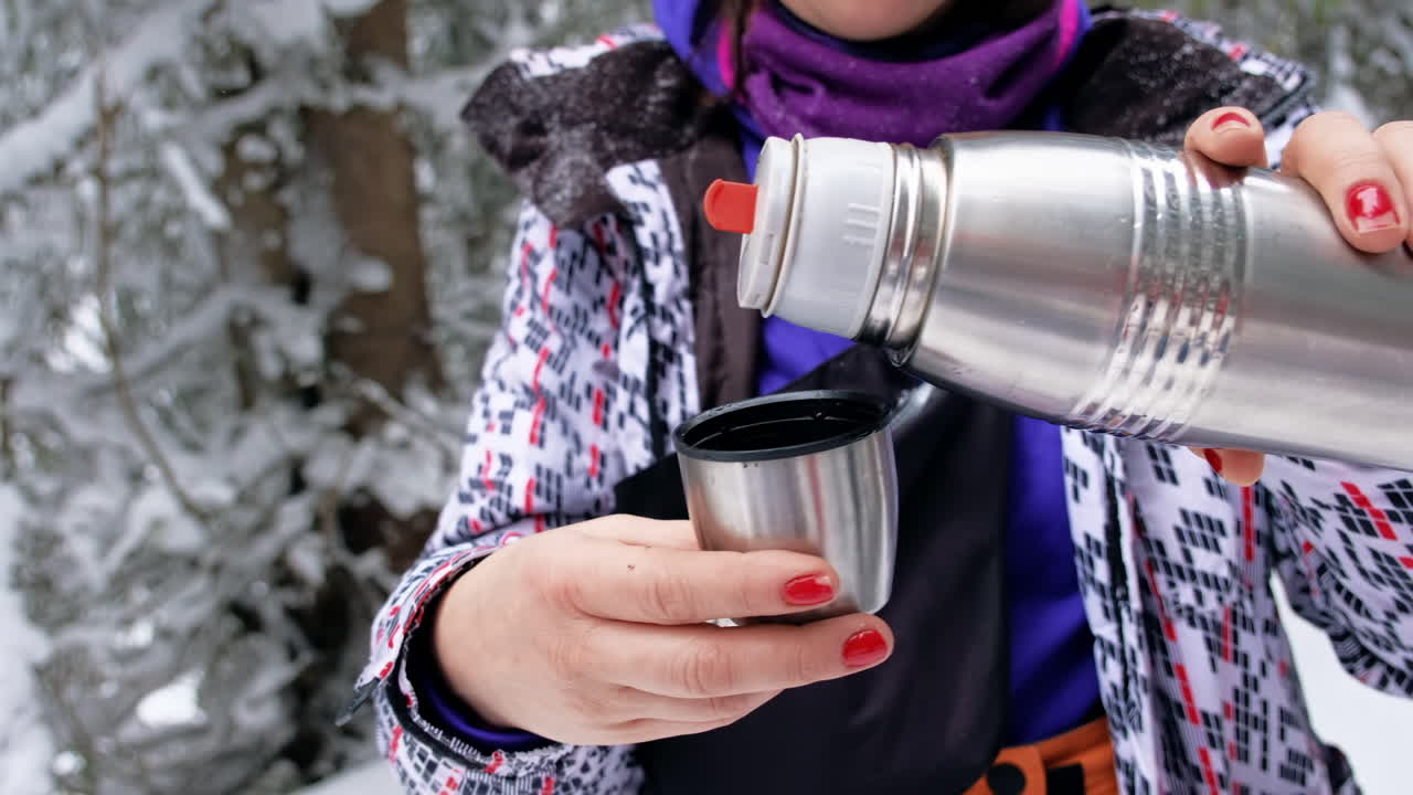 Woman pours water from a thermos In the winter Carpathians at hiking, Romania. Woman stopped while climbing Giumalau peak. Snow forest around