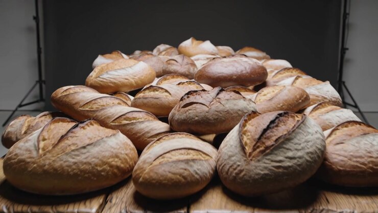 Pulling back camera revealing dense pile of artisanal loaves on wooden table, highlighting crusts