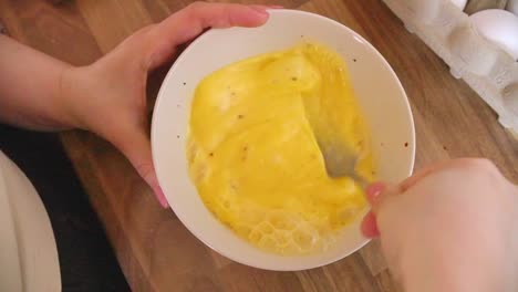 top shot woman at kitchen counter whisking an egg in bowl with a fork. handheld slow motion