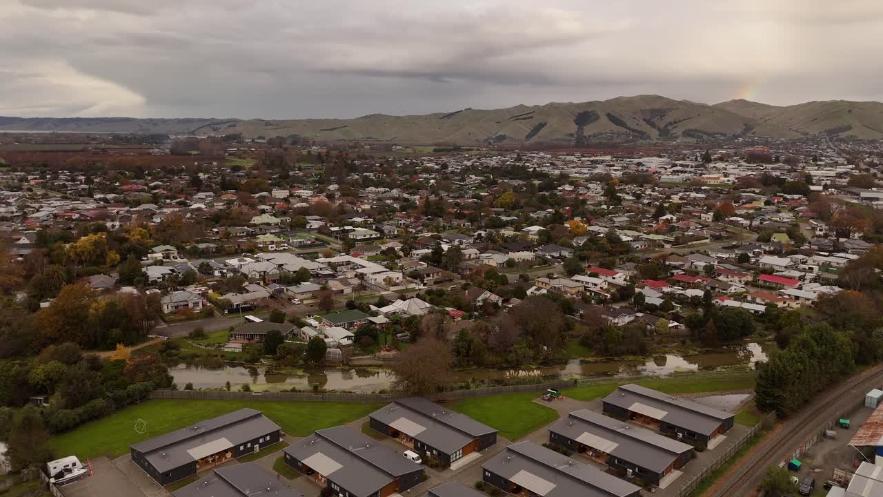 Small neighborhood In New Zealand during cloudy day. Aerial wide shot. Mountains and river flowing through city. Blenheim, South Island