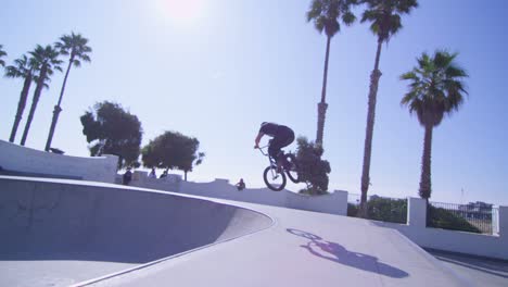 un ciclista de bmx ejecuta dos saltos altos y recorre las paredes en un skatepark