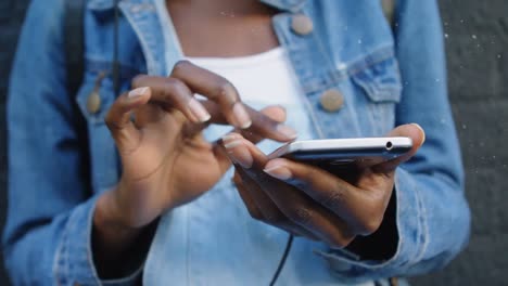 animation of snowfall over midsection of african american woman using cellphone