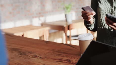 sección media de una mujer afroamericana pagando por un café para llevar con tarjeta de crédito, en cámara lenta.