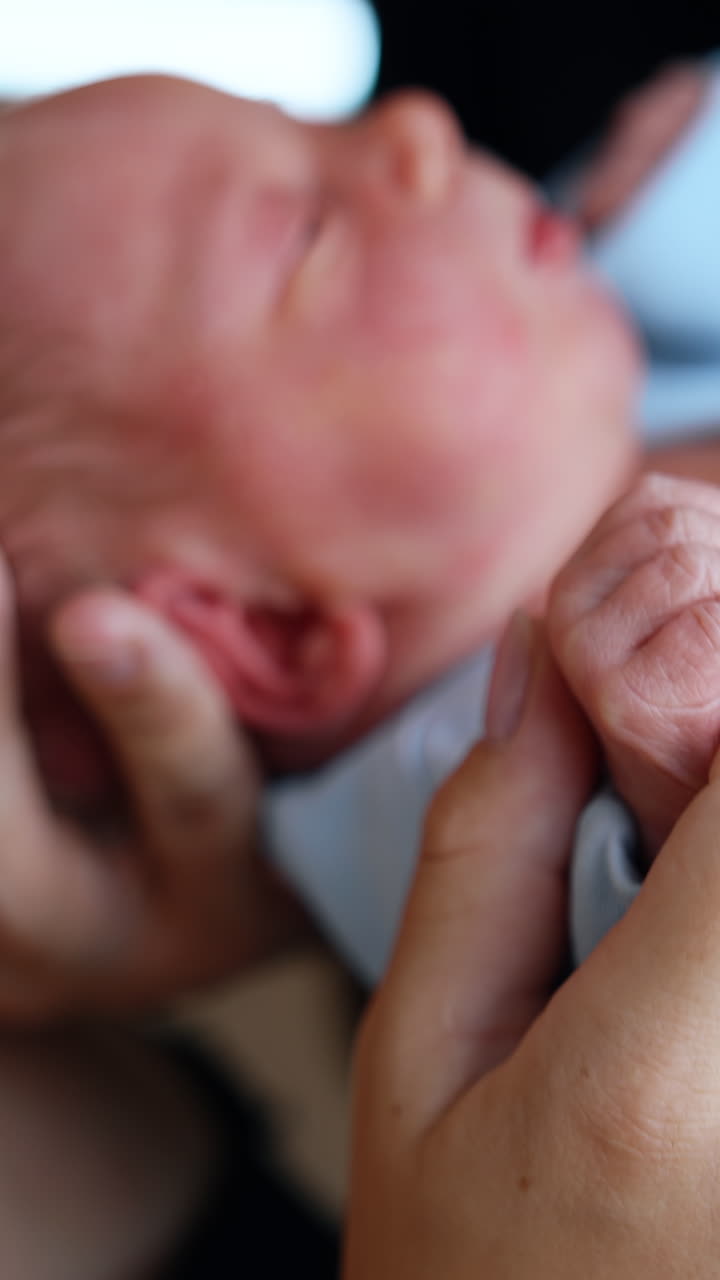 Little newborn in the secure hands of his parents. Mother kissing her adorable baby on the head. Close up. Blurred backdrop. Vertical video