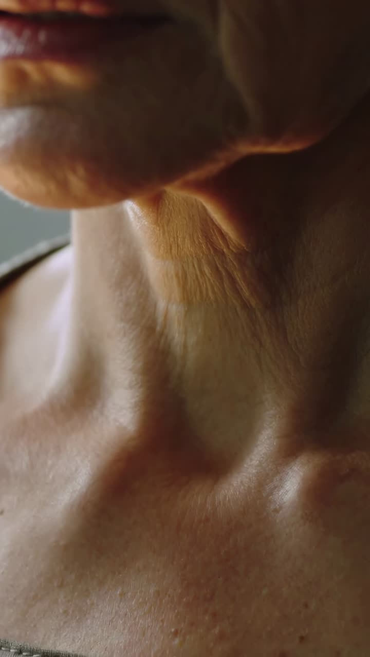 Video verticale: donna che respira muovendo la mascella e inclinando il collo in una stanza illuminata a sinistra, spallina superiore e clavicole