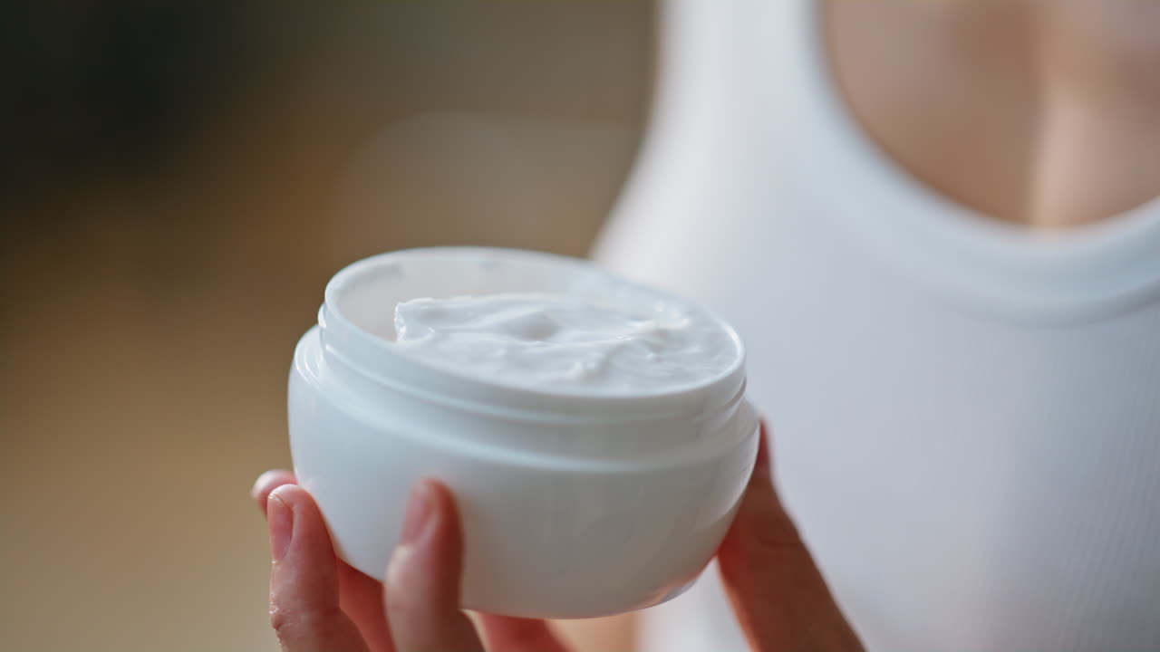 White cream elegant jar holded by woman hands indoors closeup. Unknown lady