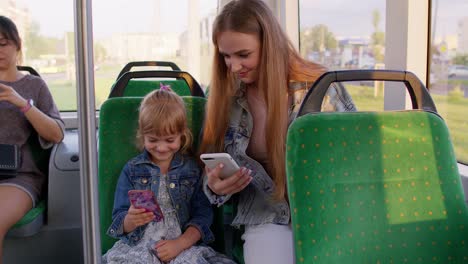 Child-girl-with-mother-using-mobile-phone-internet-social-network-application-while-traveling-by-bus