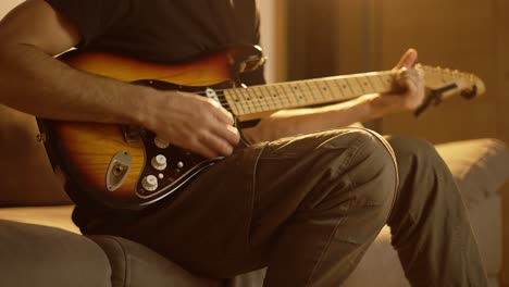 man plays the guitar while sitting on the couch