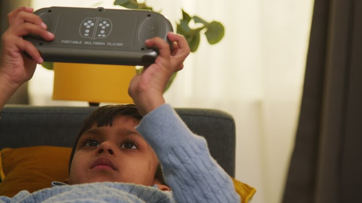 Ragazzo giovane sdraiato sul divano a casa che gioca o guarda contenuti in streaming su un dispositivo di gioco portatile