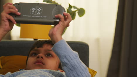 young boy lying on sofa at home playing game or streaming onto handheld gaming device