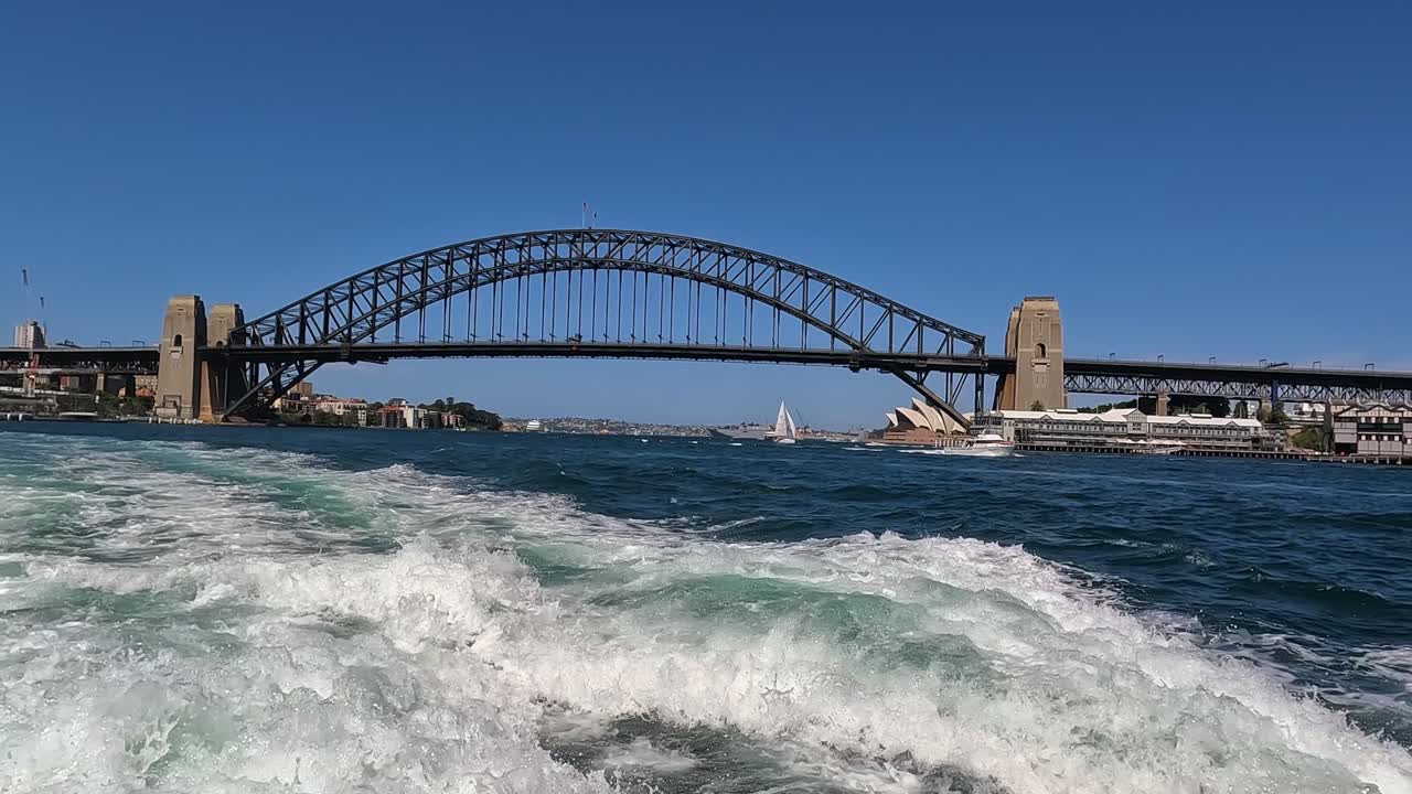 el puente del puerto de sídney y la casa de la ópera en la distancia vista desde detrás de la estela del barco